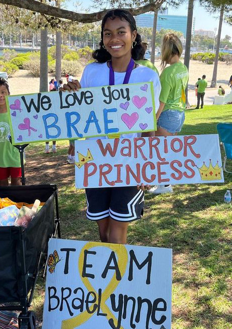 Braelynne holds a sign saying she is a "warrior princess." 