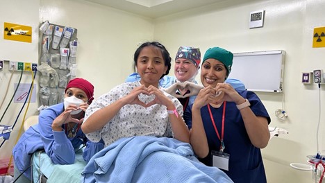 Dr. Varma and team hold up their hands in a heart shape with pediatric patient.